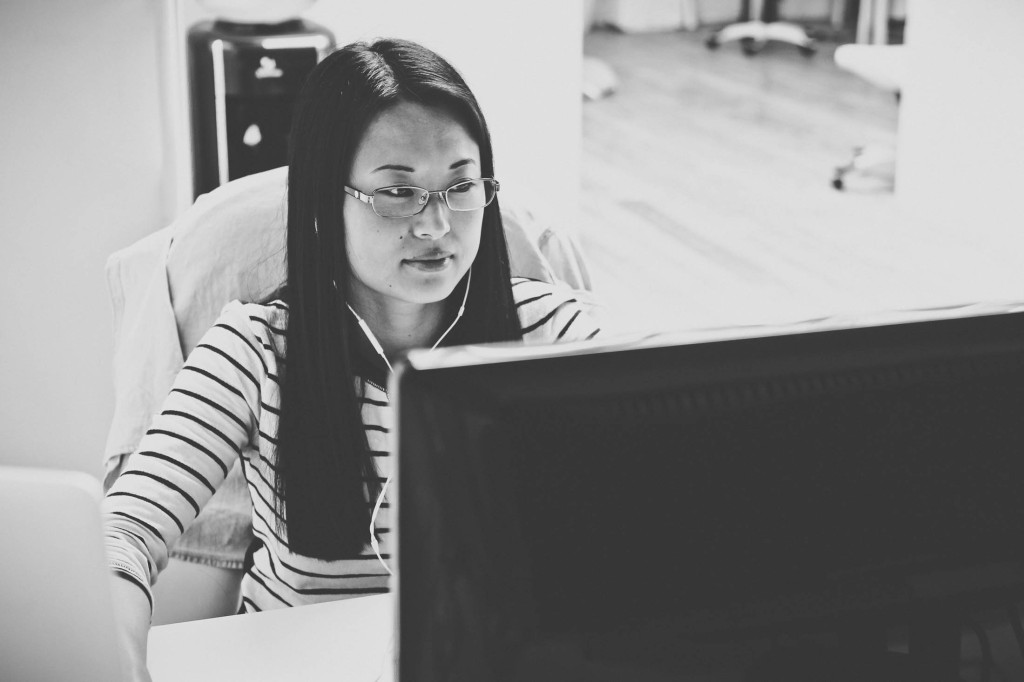 Black and white photo of a woman working at a computer with earbuds in