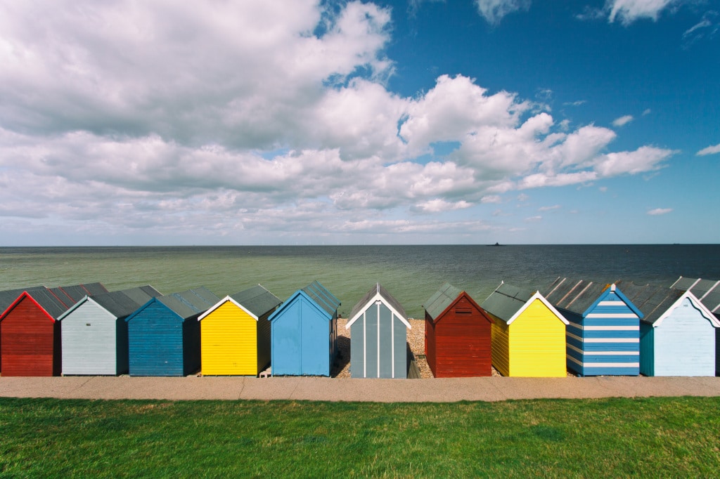 A row of sunny summer beach huts all with different, vibrant paint colors