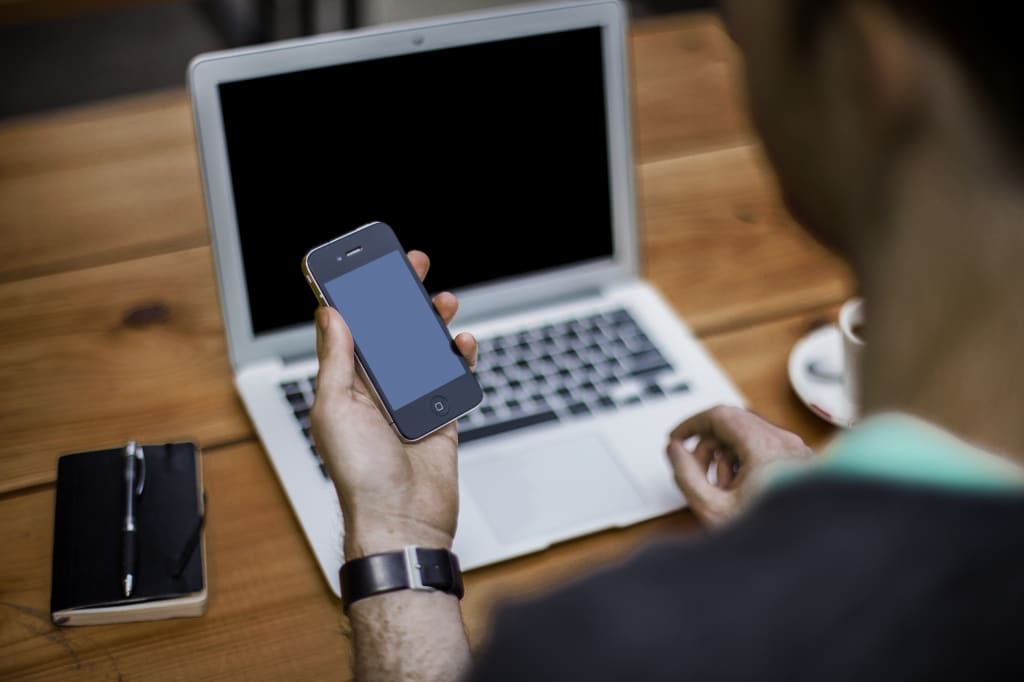 a man looks at an iPhone while seated at his laptop