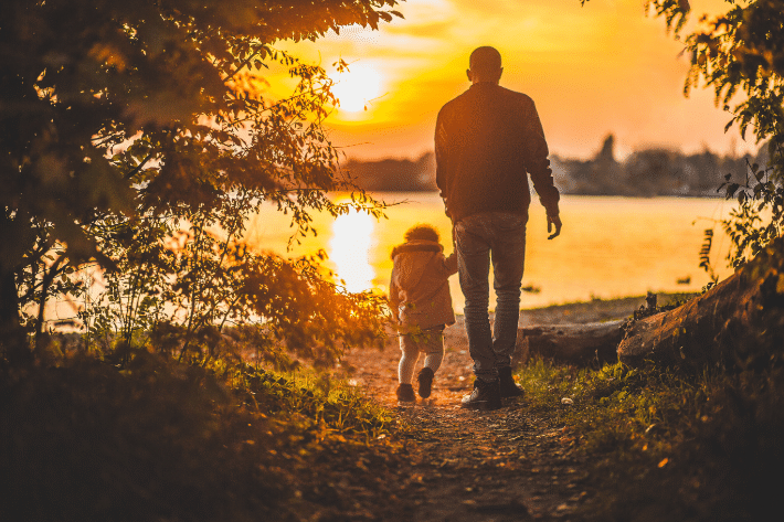 a man walks on a nature trail with a young child as the sun sets