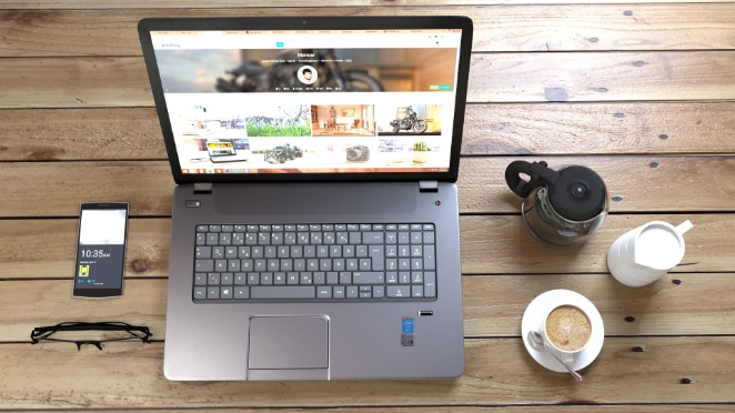 overhead view of a laptop on a desk with a phone, glasses, and coffee