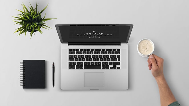 a desk with a laptop, plant, journal, and coffee cup