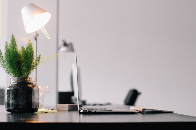 a clean desk space with a laptop, keyboard, lamp, and a small plant