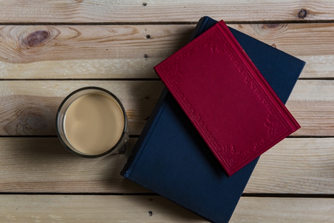 two notebooks stacked atop one another. A smaller, decorative red notebook is atop a larger, navy blue notebook. Both sit next to a cup of coffee with creamer