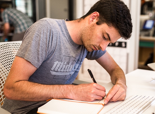 man in grey shirt writing in orange journal