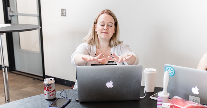 woman with hands extended over laptop and coffee at desk