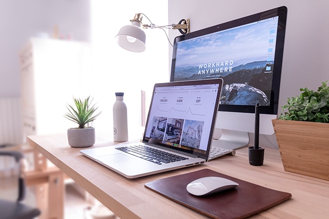 laptop desk top and phone sitting on desk with plants and lamp in background