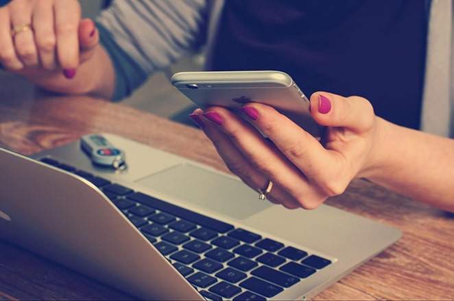 woman holding iphone and macbook laptop on desk