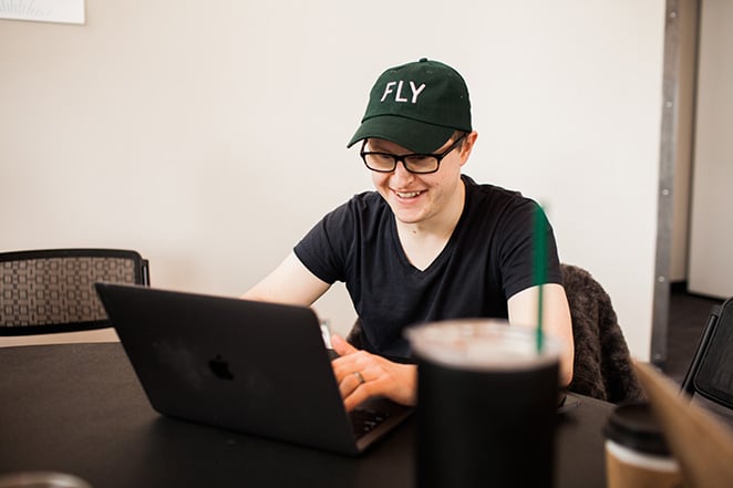 man with simple shirt and table with laptop and baseball hat