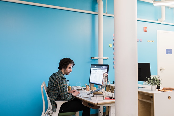 man coding at desk near bright blue wall