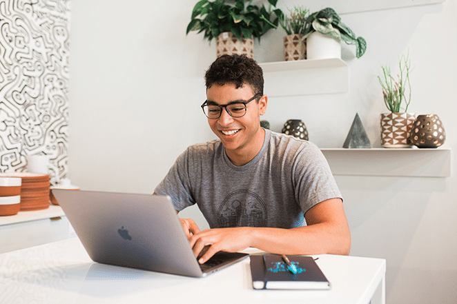 person in bright white space on laptop and with notebook nearby 