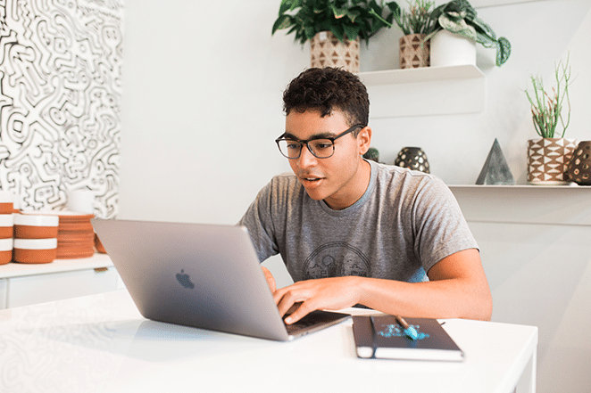 person in bright white space on laptop and with notebook nearby 