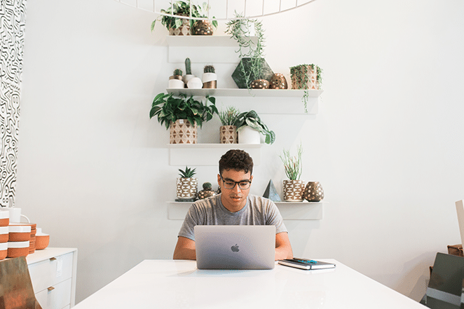 person in bright white space on laptop and with notebook nearby 